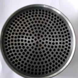 Metalowy element z regularnym wzorem otworów, ujęty z góry, prezentujący precyzję wykonania i symetryczny układ perforacji w okrągłej ramie.