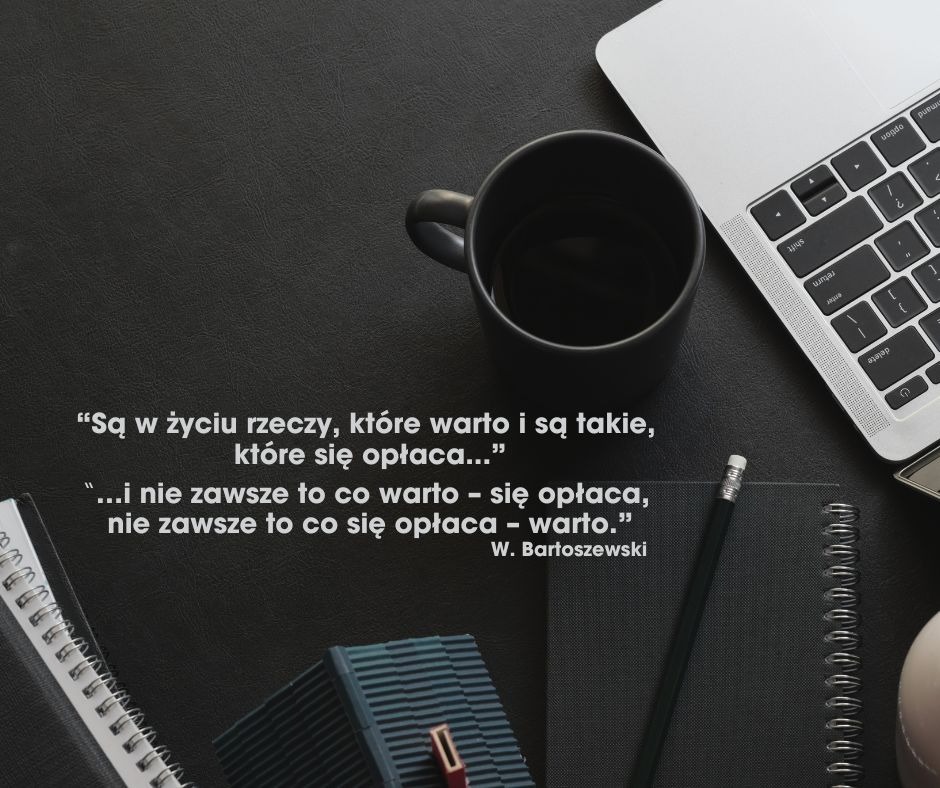 Minimalistyczne biurko z cytatem Bartoszewskiego, czarnym kubkiem, notatnikiem i laptopem. Stonowana kolorystyka i prosta kompozycja.