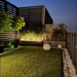 Nowoczesny ogród na dachu z oświetleniem LED pod roślinami, kulami świetlnymi i żwirowym obrzeżem. Widoczne elementy konstrukcji i roślinność.