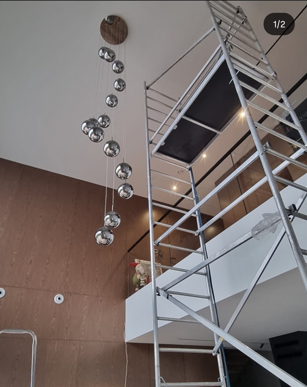 Wysoka drabina przy nowoczesnej lampie kulistej w przestronnym wnętrzu z drewnianą ścianą. Widoczne punkty oświetleniowe w suficie.