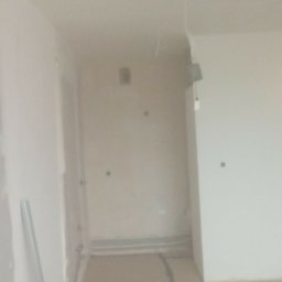 Pios karol - Wnętrze w trakcie prac wykończeniowych: ściany przygotowane do malowania, widoczne narzędzia i materiały budowlane. Fragment podłogi z poziomowaniem.