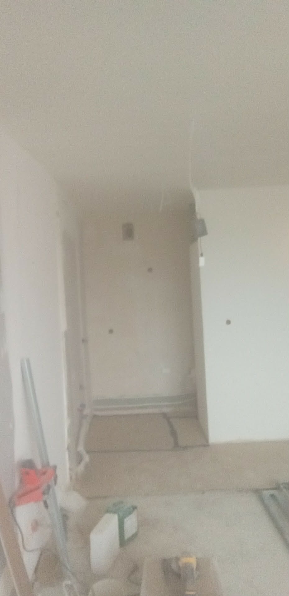 Wnętrze w trakcie prac wykończeniowych: ściany przygotowane do malowania, widoczne narzędzia i materiały budowlane. Fragment podłogi z poziomowaniem.