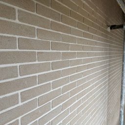 Mykonta Company Sp z oo - Ściana z cegieł klinkierowych w odcieniach beżu, z widocznymi białymi fugami, sfotografowana pod kątem z rusztowaniem w tle.