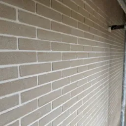 Ściana z cegieł klinkierowych w odcieniach beżu, z widocznymi białymi fugami, sfotografowana pod kątem z rusztowaniem w tle.