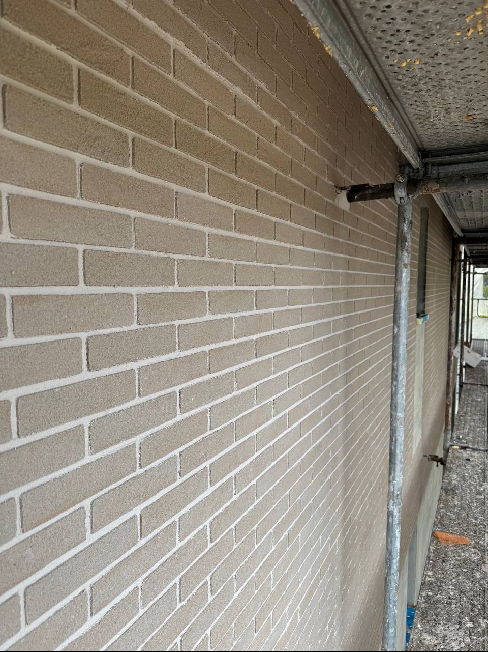 Elewacja budynku wykończona w stylu cegieł, z widocznymi rusztowaniami. Jasna kolorystyka i wyraźna faktura cegieł. Perspektywa boczna.