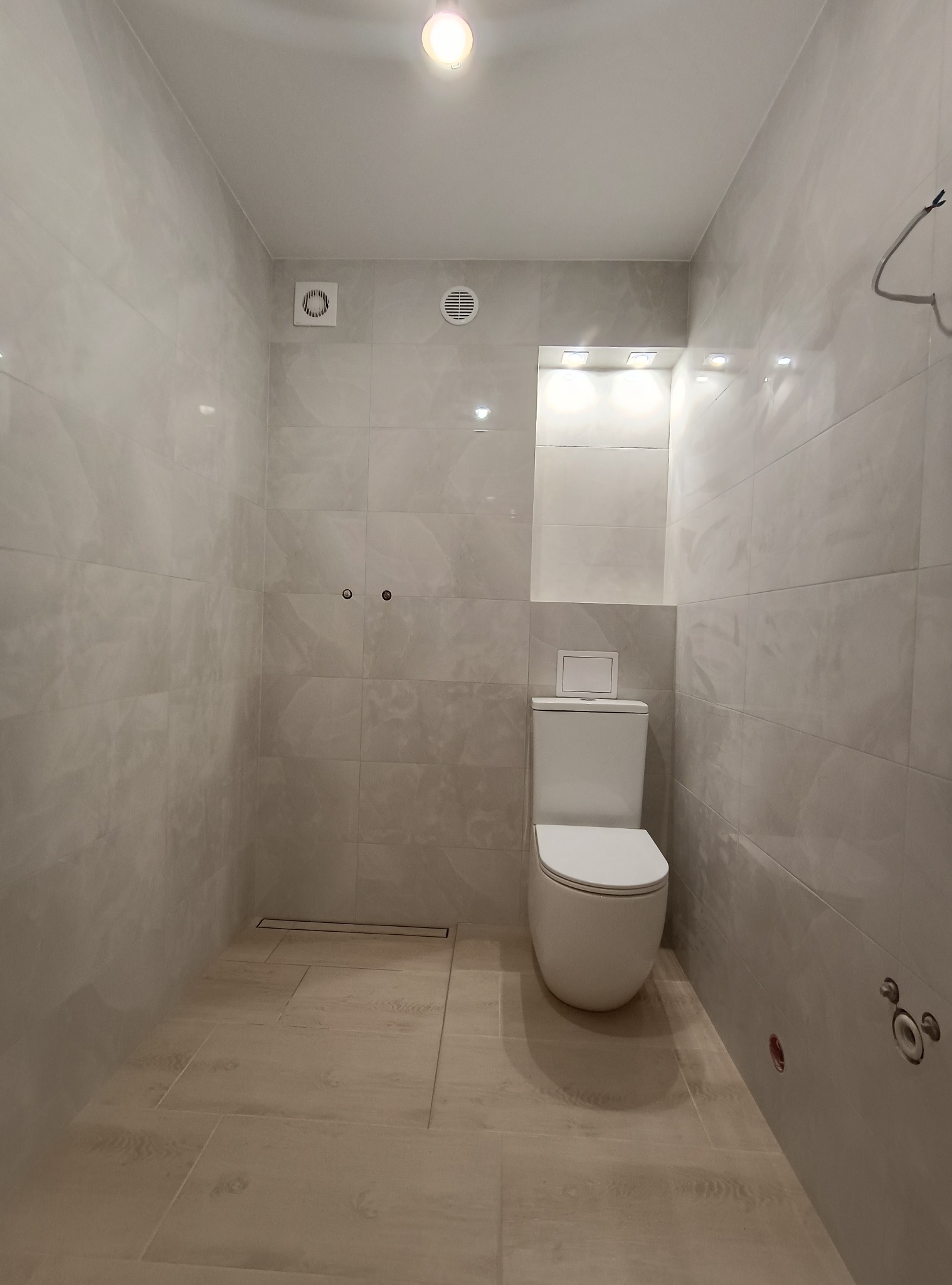 Jasna łazienka po remoncie: beżowe płytki na podłodze i ścianach, biała toaleta, minimalistyczny design, oświetlenie sufitowe i wnękowe. Widoczne detale wykończeniowe.