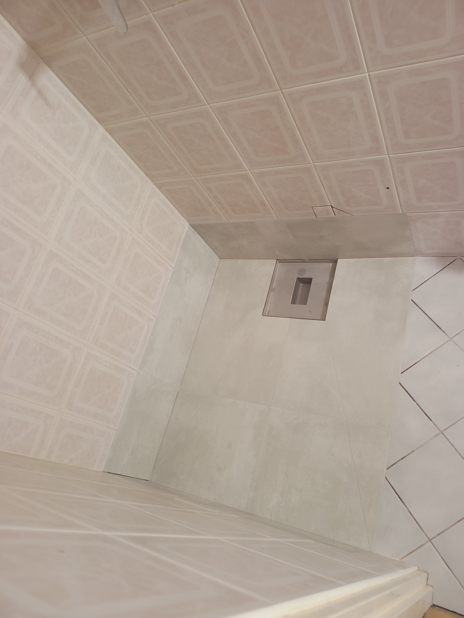 Wykończona łazienka z beżowymi płytkami na ścianach i podłodze, widoczny odpływ liniowy. Minimalistyczny design, jasne wnętrze. Ukończony etap prac.