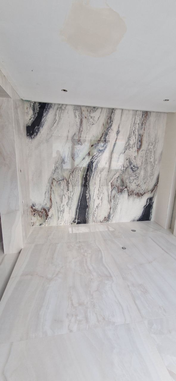 Wykończona łazienka z marmurowymi płytami na ścianach i podłodze. Widoczne czarne i brązowe żyły w białym marmurze. Na suficie widoczne ślady po zalaniu.