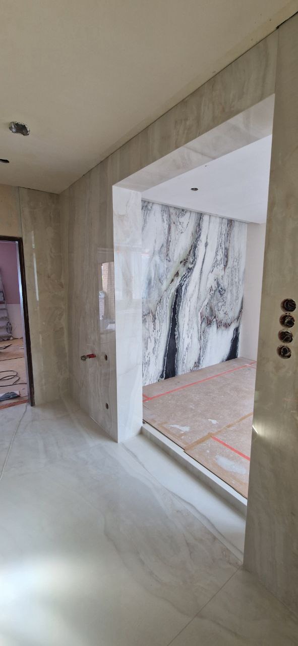 Łazienka w trakcie wykończenia: marmurowe płytki na ścianie, podłoga wyłożona jasnymi płytkami imitującymi marmur. Widoczne przygotowania do dalszych prac.