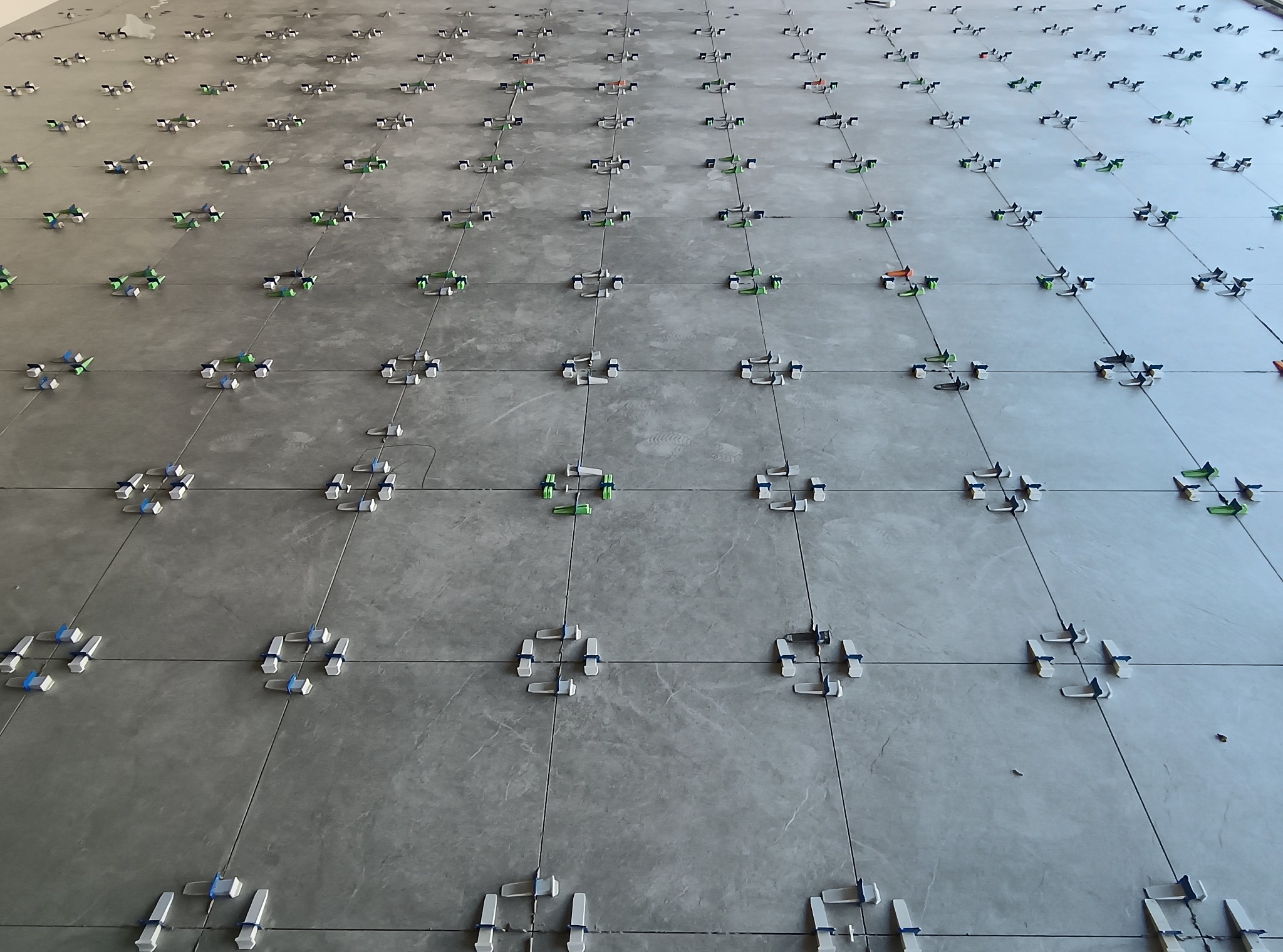 Szare płytki podłogowe ułożone z użyciem systemu poziomowania, widoczne kliny i klipsy dystansowe. Układanie płytek w trakcie realizacji.