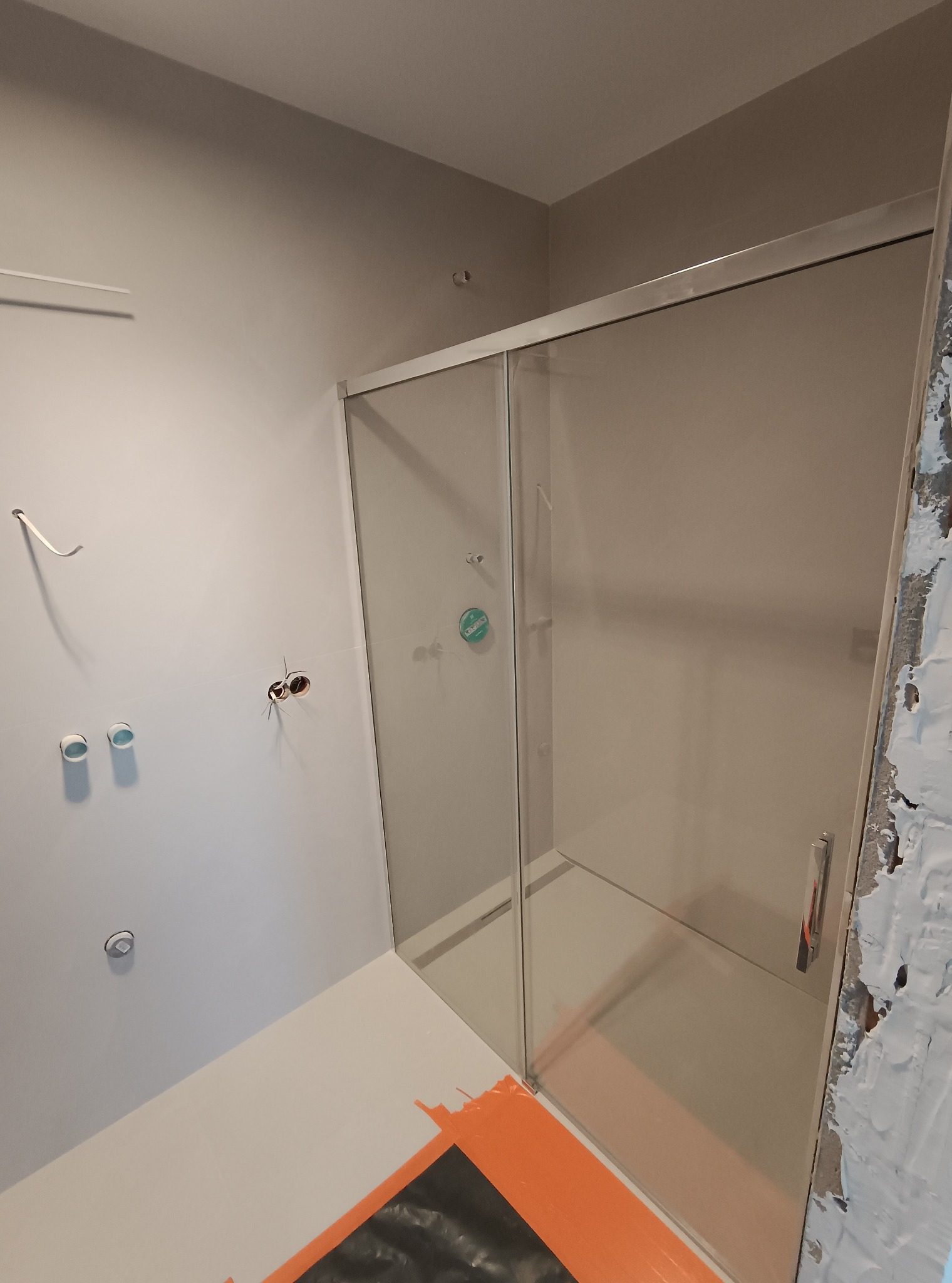 Nowoczesna kabina prysznicowa z przesuwnymi drzwiami, zamontowana w łazience w trakcie wykończenia. Widoczne przygotowane instalacje i zabezpieczona podłoga.