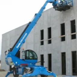 Niebieski podnośnik koszowy Genie GTH-4018SR przy szarej, betonowej ścianie budynku z otworami okiennymi. Na platformie roboczej dwóch pracowników w kaskach.