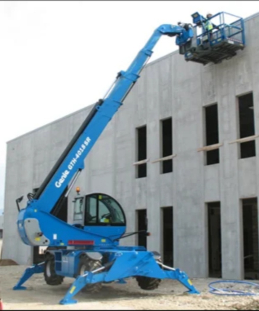 Niebieski podnośnik koszowy Genie GTH-4018SR przy szarej, betonowej ścianie budynku z otworami okiennymi. Na platformie roboczej dwóch pracowników w kaskach.