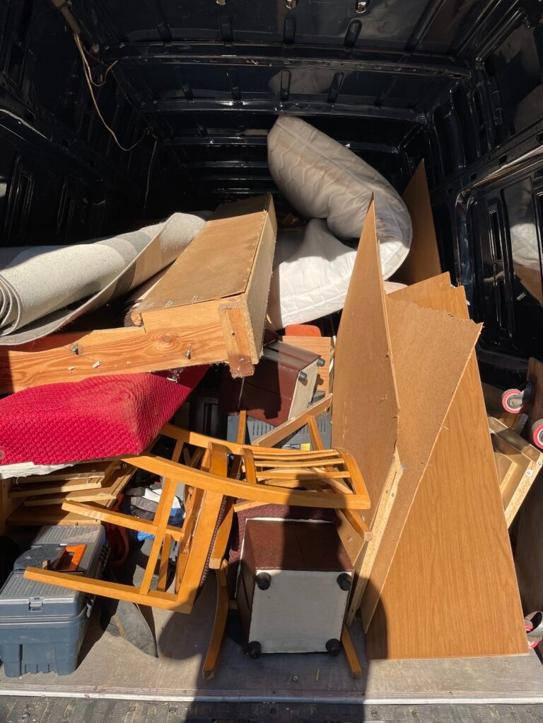 Wnętrze furgonetki załadowanej meblami, materacem i dywanami, gotowymi do transportu lub utylizacji podczas opróżniania mieszkania. Widok z tylnych drzwi.