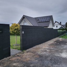 BRUKIO MICHAŁ JABŁOŃSKI - Nowoczesne ogrodzenie betonowe z numerem domu '5 Grafitowa' na tle domu z panelami słonecznymi i zadbanego trawnika.