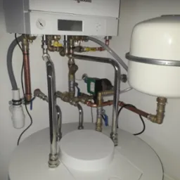 Biały piec Viessmann z licznymi rurami miedzianymi i zaworami, zamontowany na okrągłym zbiorniku. Widoczne elementy instalacji grzewczej.