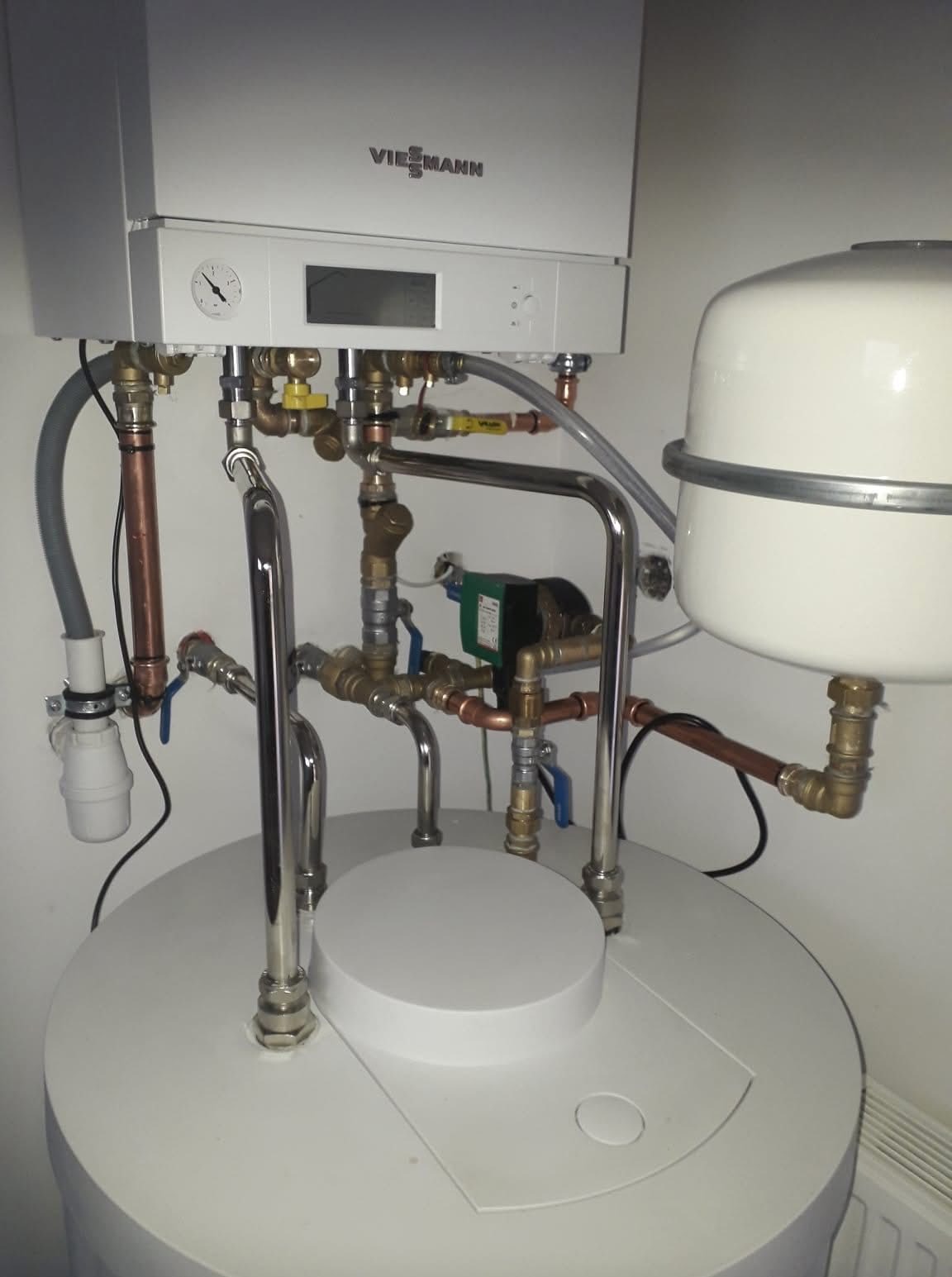 Biały piec Viessmann z licznymi rurami miedzianymi i zaworami, zamontowany na okrągłym zbiorniku. Widoczne elementy instalacji grzewczej.