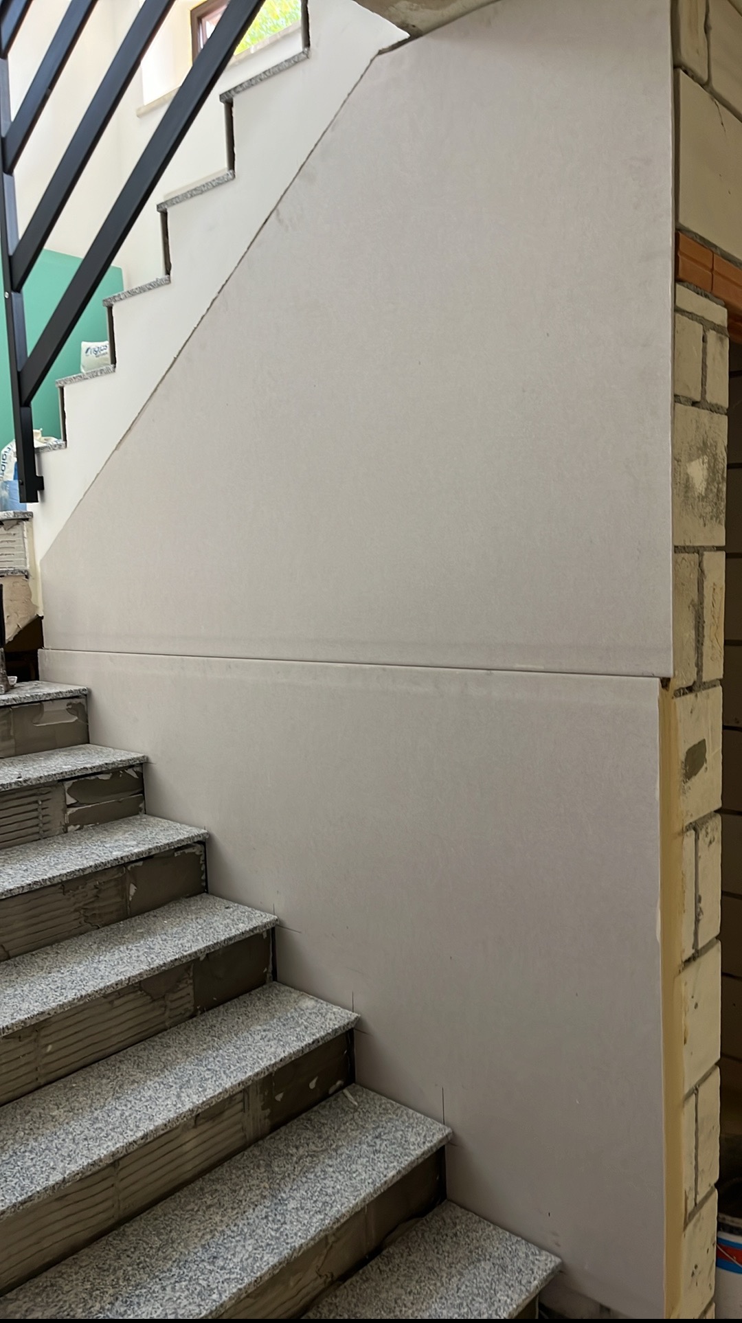 Ściana przy schodach w trakcie montażu płyty karton gips. Widoczne płyty na ścianie i fragment schodów z szarego kamienia.