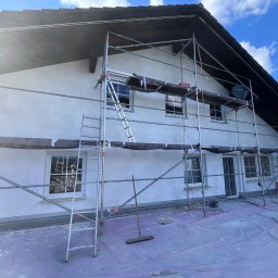 TynkMaksBud - Dom jednorodzinny w trakcie prac elewacyjnych, widoczne rusztowanie, świeżo nałożony tynk i zabezpieczona folią przestrzeń robocza.