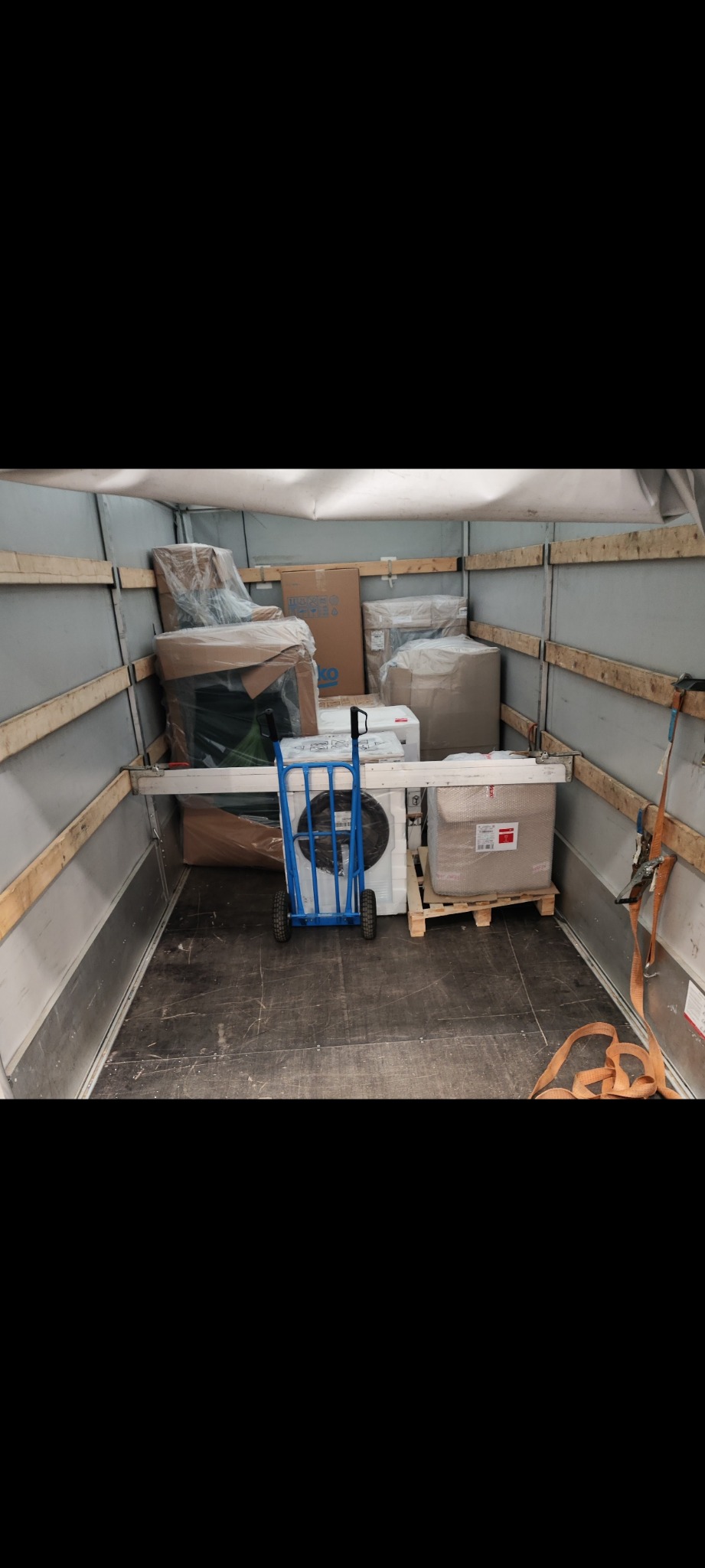 Wnętrze busa załadowane meblami i sprzętem AGD do przeprowadzki. Widoczny wózek transportowy i zabezpieczone kartony.