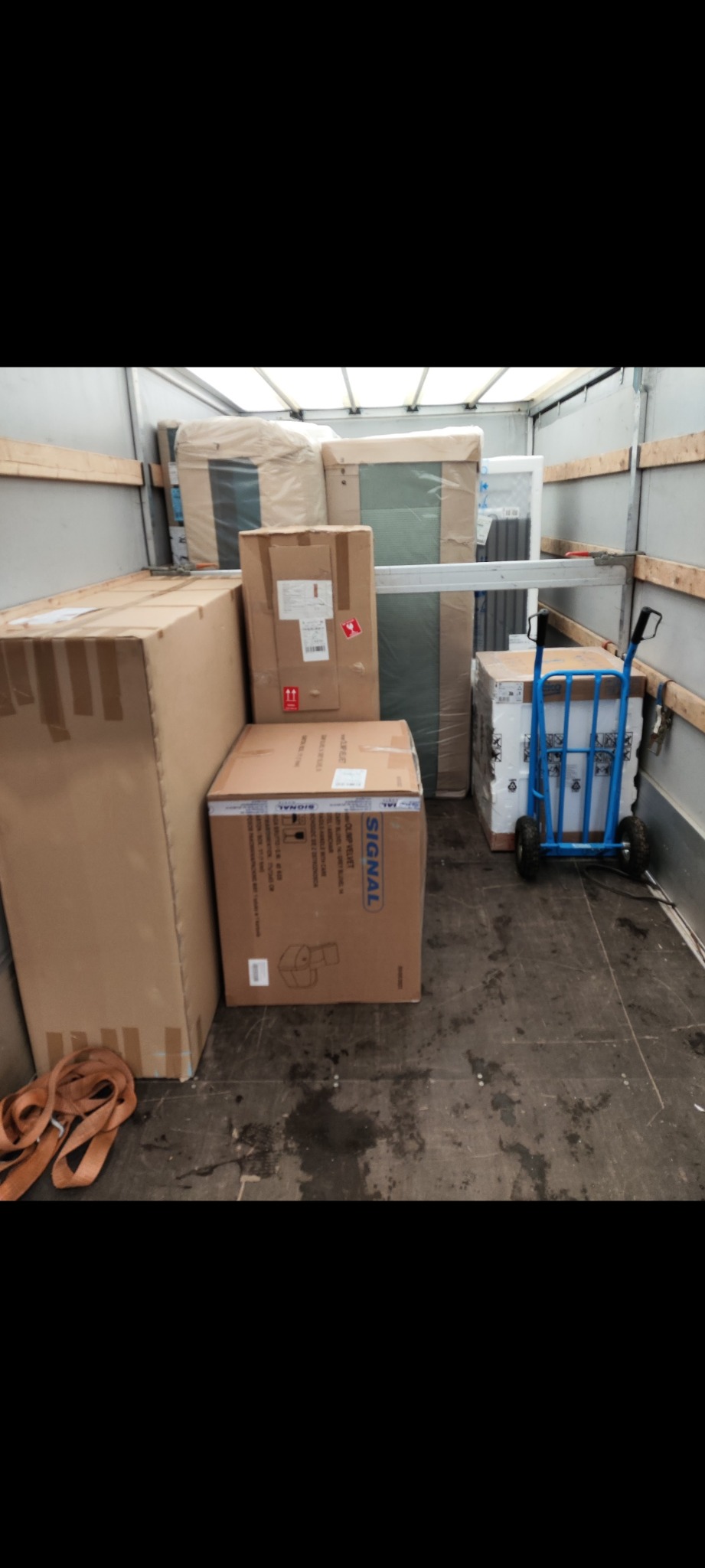 Wnętrze busa wypełnione kartonami i meblami gotowymi do transportu. Widoczny wózek transportowy i pasy zabezpieczające ładunek.