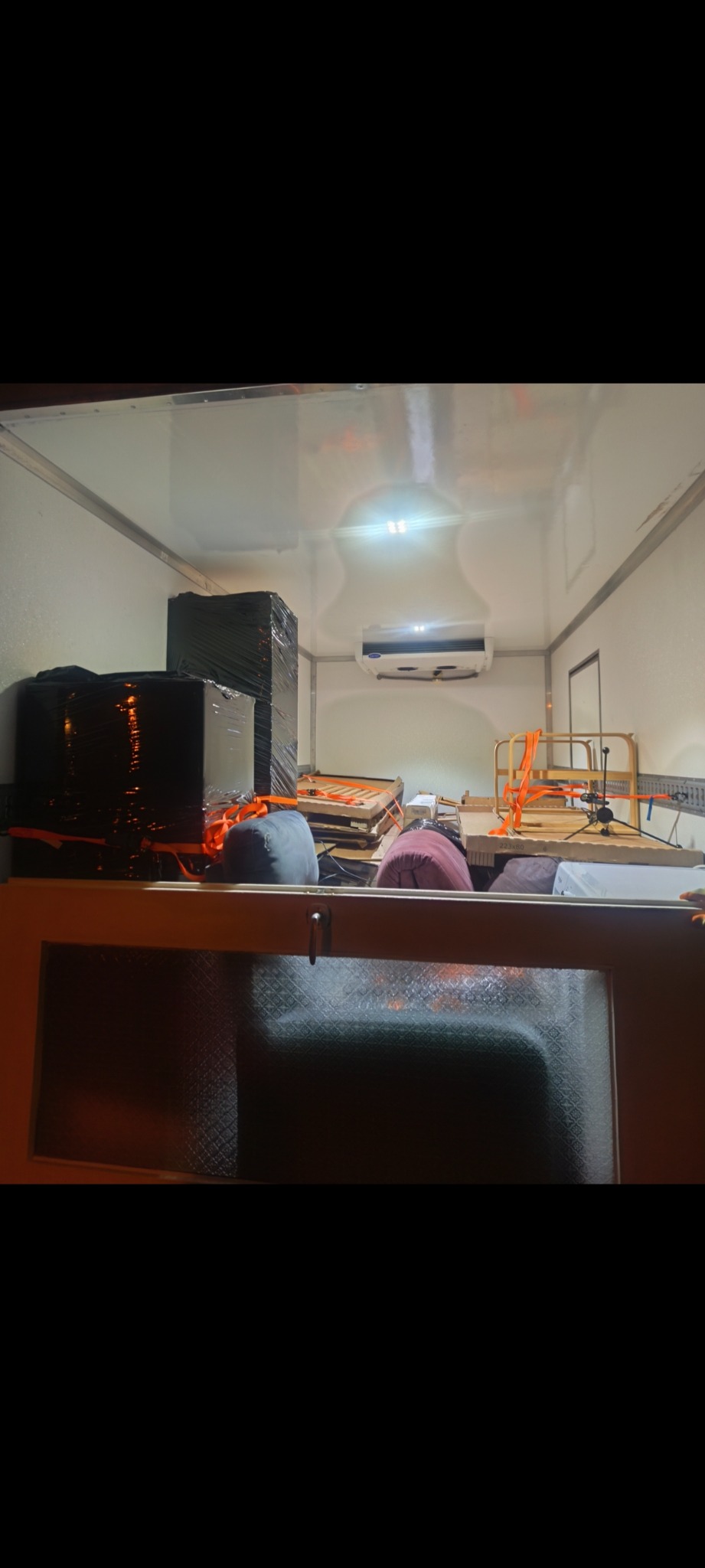 Wnętrze chłodni transportowej wypełnione zabezpieczonymi meblami i sprzętami, gotowymi do przewozu. Widoczne pasy mocujące i klimatyzacja.