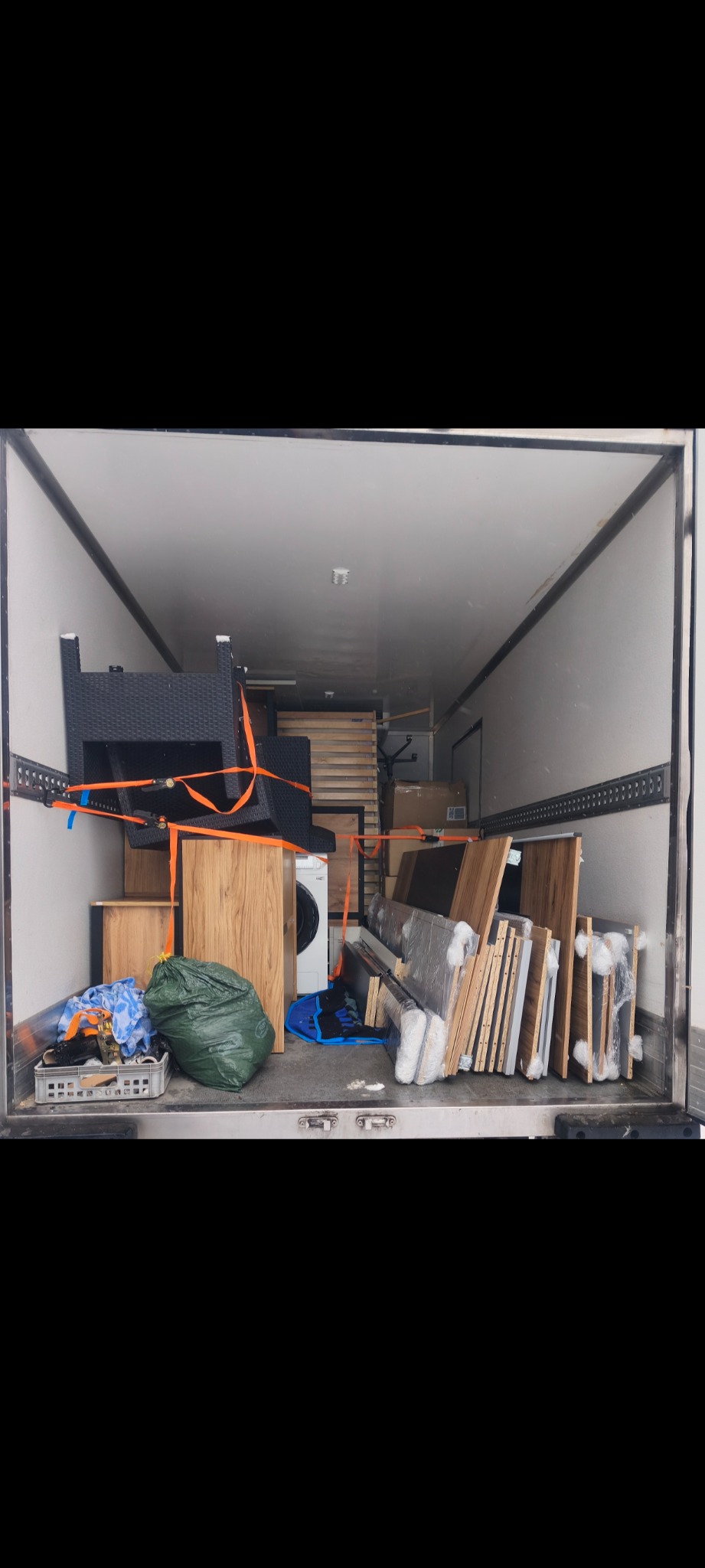 Wnętrze busa wypełnione meblami, sprzętem AGD (pralka) i spakowanymi rzeczami, zabezpieczonymi pasami transportowymi. Widok z tyłu pojazdu.