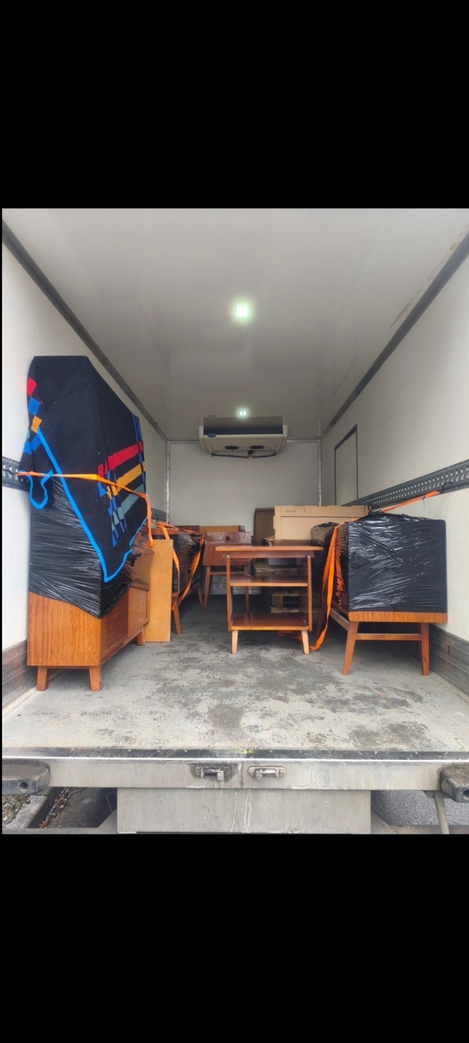 Wnętrze chłodni transportowej wypełnione meblami zabezpieczonymi folią i pasami, gotowymi do przewozu. Widoczne komody, stoliki i krzesła.