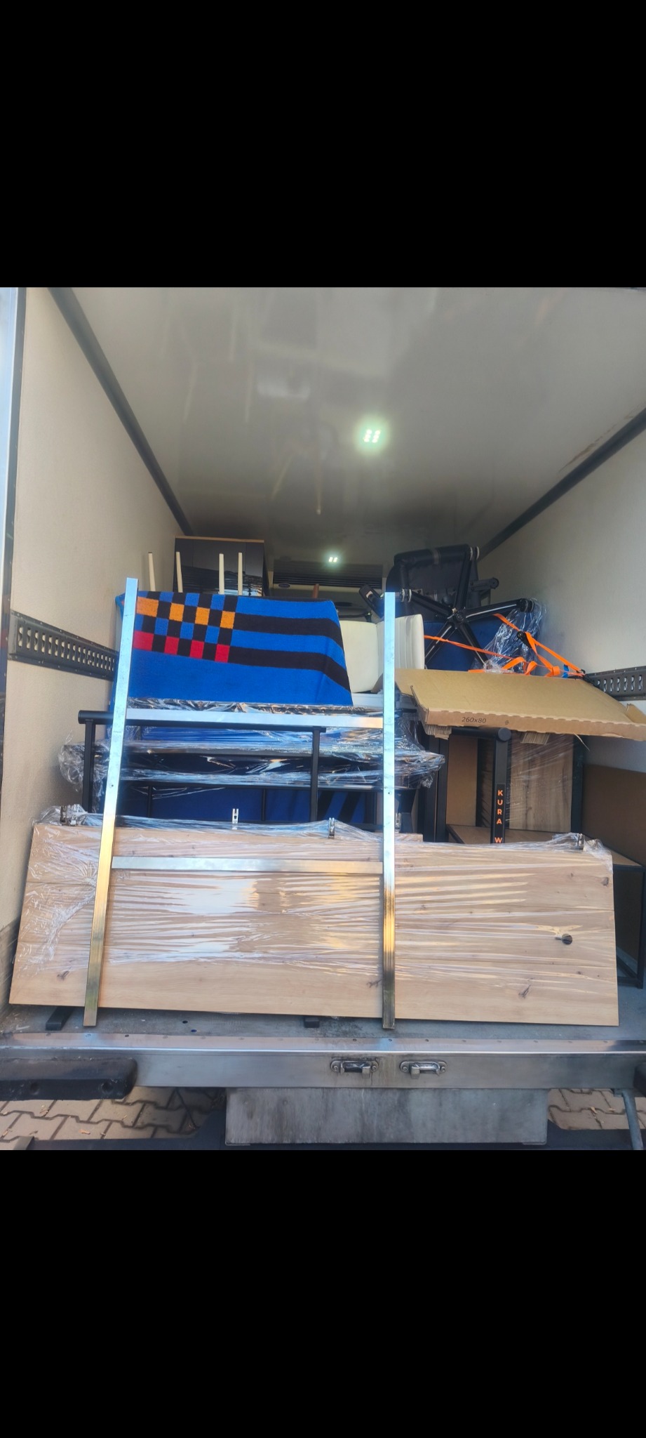 Wnętrze busa załadowane meblami i przedmiotami, przygotowanymi do transportu. Widoczne zabezpieczenia folią i pasami.