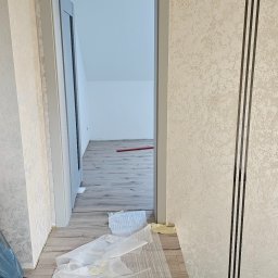Marcin Stępień - Remont pokoju: widok na świeżo położone panele podłogowe przez szare futryny drzwiowe. Na ścianie dekoracyjna tapeta z czarnymi paskami.