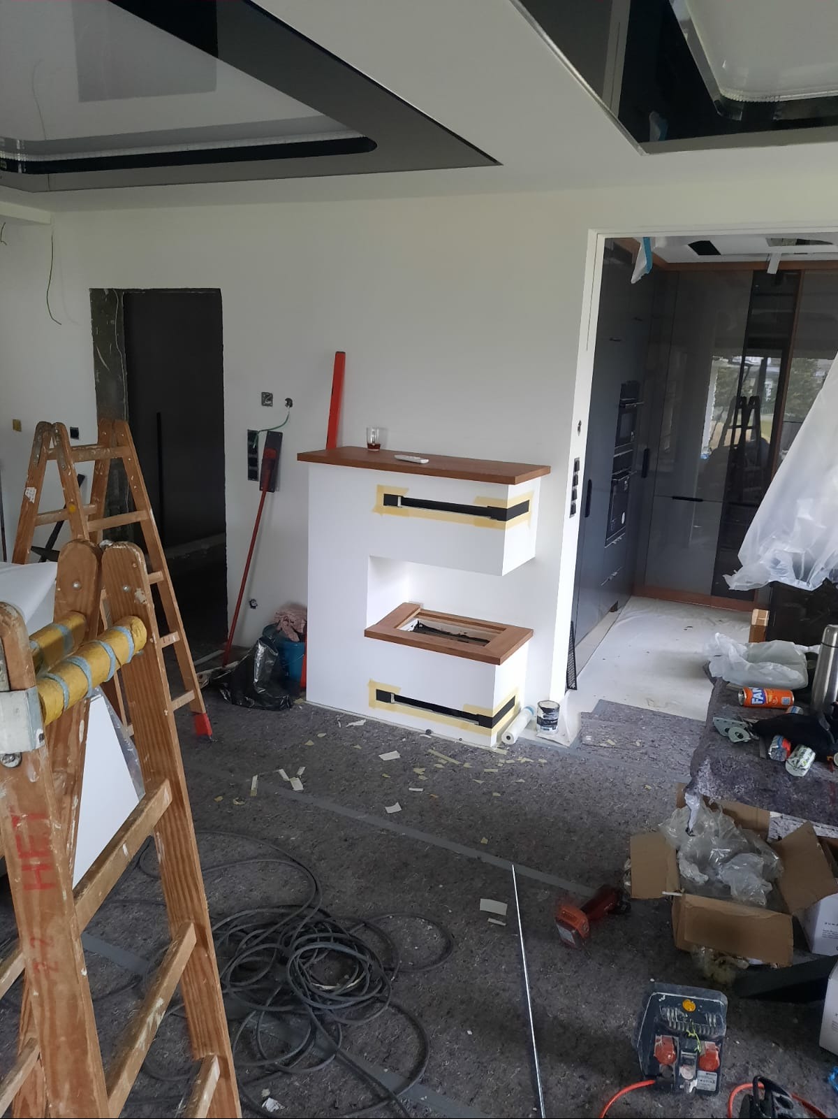 Wnętrze w trakcie prac remontowych. Widoczne schody, drabina, elementy dekoracyjne sufitu i ściany. Na podłodze zabezpieczenia i narzędzia.