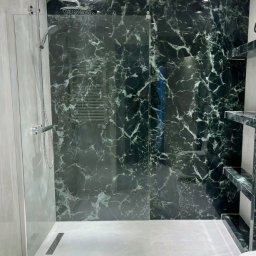 Kompleksowe Remonty - Wykończona łazienka z kabiną typu walk-in, wyłożona płytkami imitującymi zielony marmur. Widoczny odpływ liniowy i półki z tego samego materiału.