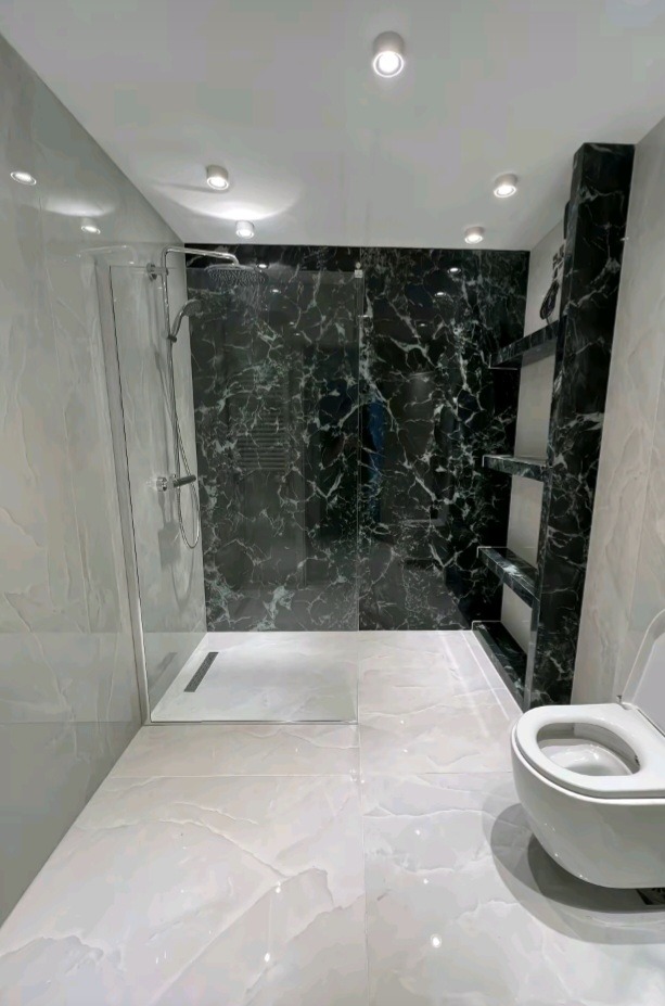 Nowoczesna łazienka po remoncie: kabina prysznicowa typu walk-in, marmurowe płytki w odcieniach bieli i czerni, podświetlane półki w ścianie, biała toaleta.