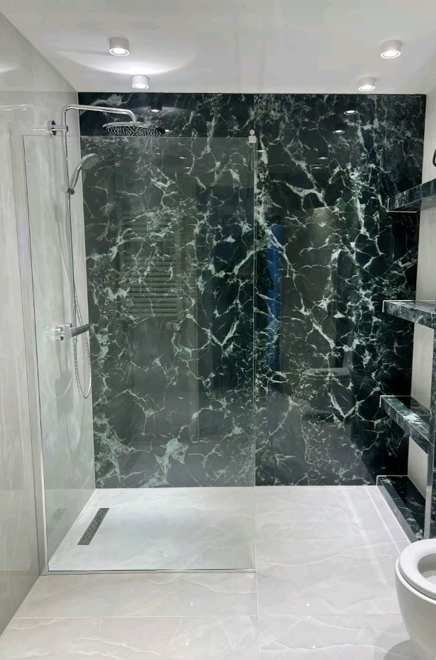 Wykończona łazienka z kabiną typu walk-in, wyłożona płytkami imitującymi zielony marmur. Widoczny odpływ liniowy i półki z tego samego materiału.