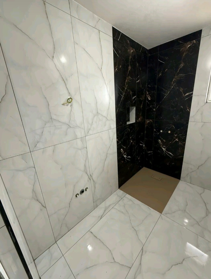 Wykończona kabina prysznicowa z białymi i czarnymi płytkami imitującymi marmur. Widoczne odpływy i instalacja wodna w ścianie. Nowoczesny design łazienki.