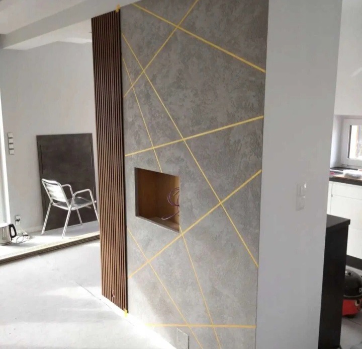 Ściana z szarą strukturą, złote linie, drewniane lamele i otwór na TV. Nowoczesne wykończenie wnętrza w surowym stylu z minimalistycznym akcentem.