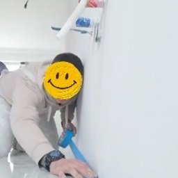 CraftGips - Pracownik zabezpiecza taśmą podłogę przy ścianie przed malowaniem. Widoczne białe płytki podłogowe i fragment instalacji na ścianie.