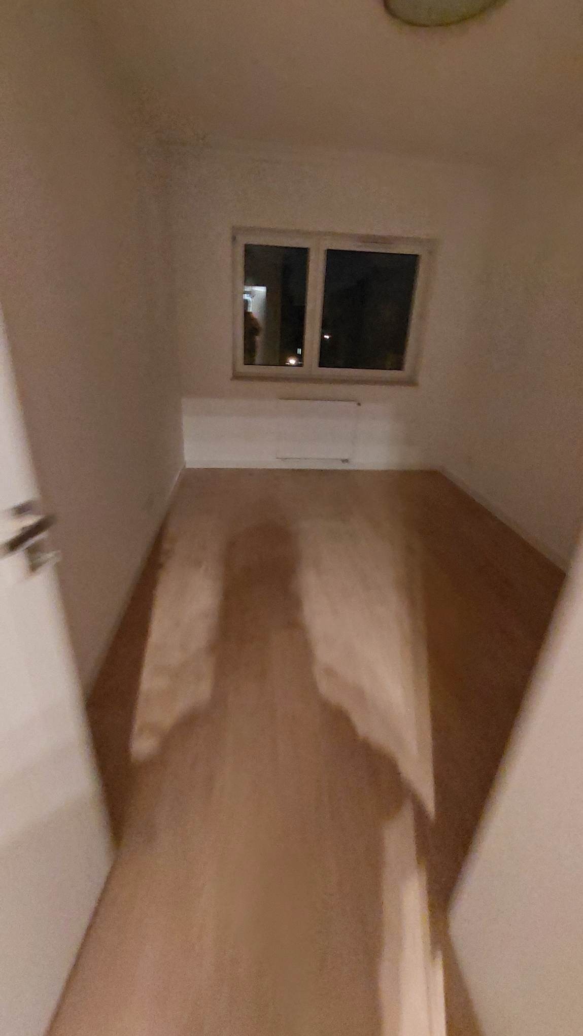 Pusty pokój po szpachlowaniu, gotowy do malowania. Widoczne gładkie ściany, okno i grzejnik. Podłoga z paneli. Otwarty kadr przez framugę drzwi.