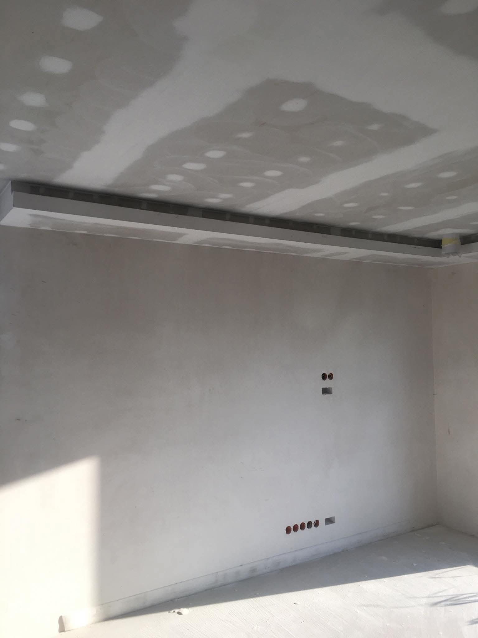 Pokój po szpachlowaniu z widoczną listwą sufitową i przygotowanymi otworami na gniazdka. Ściany i sufit w jasnych odcieniach szarości, gotowe do dalszych prac wykończeniowych.