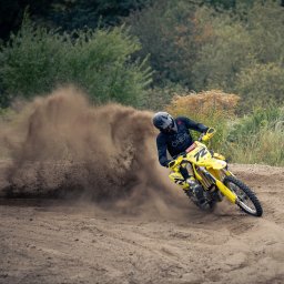 PR Graphics Zumkowski-Pawłowicz - Żółty motocykl crossowy w akcji, dynamiczne ujęcie z piaskiem w tle, zawodnik w czarnym stroju i kasku, numer 72 na maszynie. Widoczne logo fotografa.