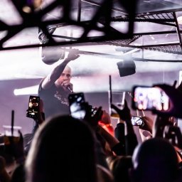 PR Graphics Zumkowski-Pawłowicz - Koncert w klubie: raper na scenie, oświetlenie, tłum fanów nagrywających występ telefonami. Widoczny fragment konstrukcji sufitu i logo klubu 'Beczka'.