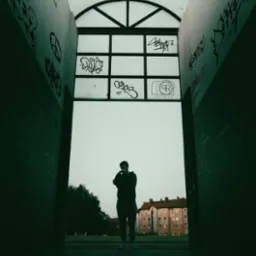 Sylwetka mężczyzny w tunelu z graffiti i logo 'QR Graphics' na szybie. Budynek mieszkalny w tle, pochmurne niebo.