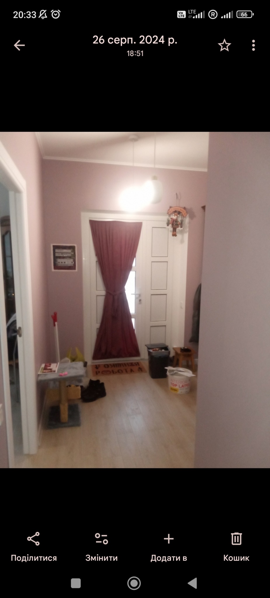 Pomieszczenie po odświeżeniu: ściany w odcieniach fioletu, jasna podłoga, białe drzwi z zasłoną. Widoczny pojemnik z farbą i dekoracje.