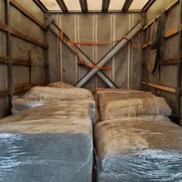 Wnętrze przestrzeni ładunkowej busa z zapakowanymi meblami, zabezpieczonymi folią stretch. Widoczne pasy mocujące i metalowe wzmocnienia ścian.