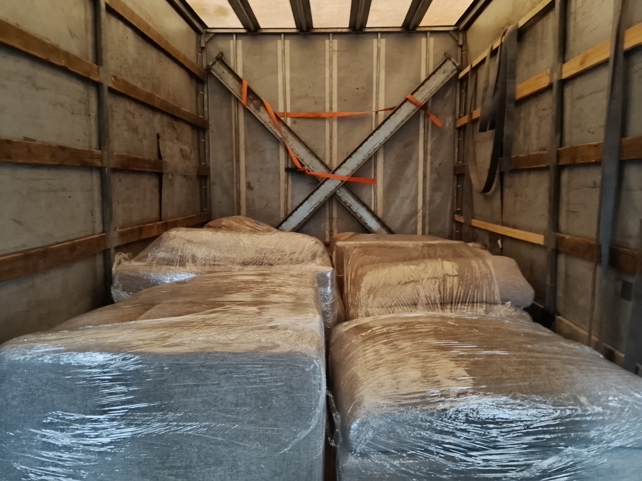 Wnętrze przestrzeni ładunkowej busa z zapakowanymi meblami, zabezpieczonymi folią stretch. Widoczne pasy mocujące i metalowe wzmocnienia ścian.