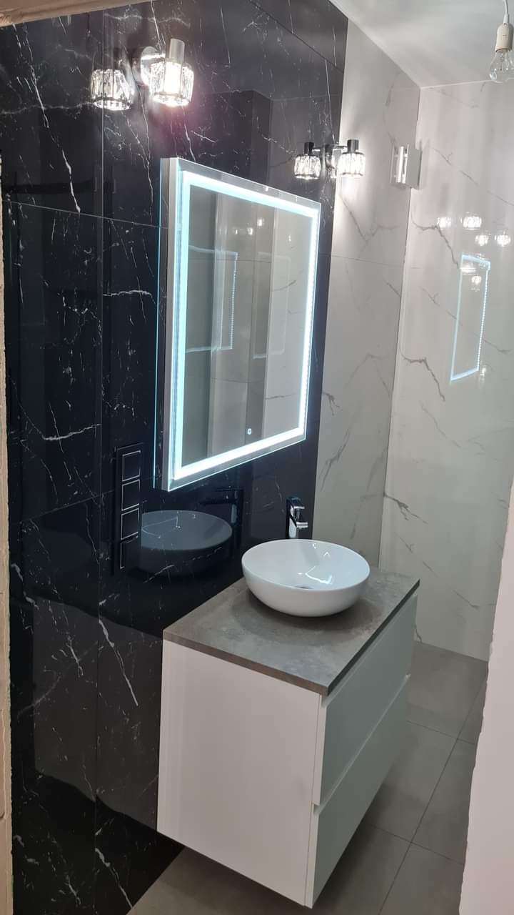 Elegancka łazienka z czarnymi i białymi płytkami imitującymi marmur, podświetlanym lustrem i białą umywalką nablatową na szafce. Nowoczesny design.
