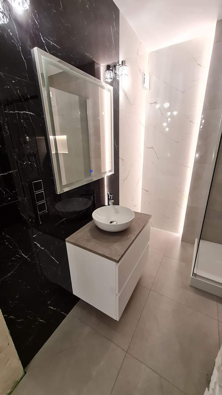 Nowoczesna łazienka z czarno-białymi marmurowymi płytkami, umywalką nablatową i podświetlanym lustrem. Minimalistyczny design, eleganckie wykończenie.