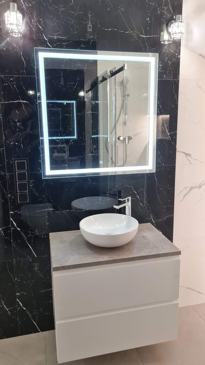 Nowoczesna łazienka: biała umywalka nablatowa, szafka z szufladami, lustro z podświetleniem LED na tle czarnych marmurowych płytek i minimalistyczna armatura.