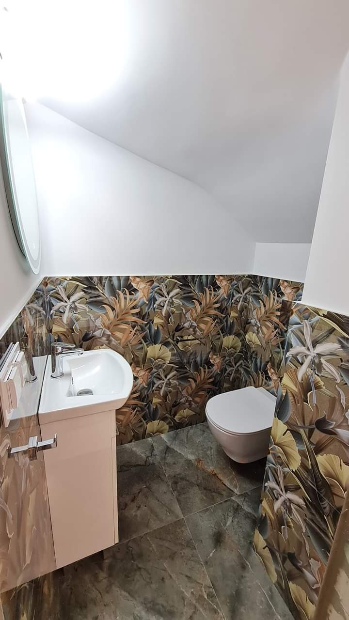 Nowoczesna łazienka na poddaszu z marmurową podłogą, umywalką na szafce i toaletą. Ściany zdobią płytki z motywem liści.