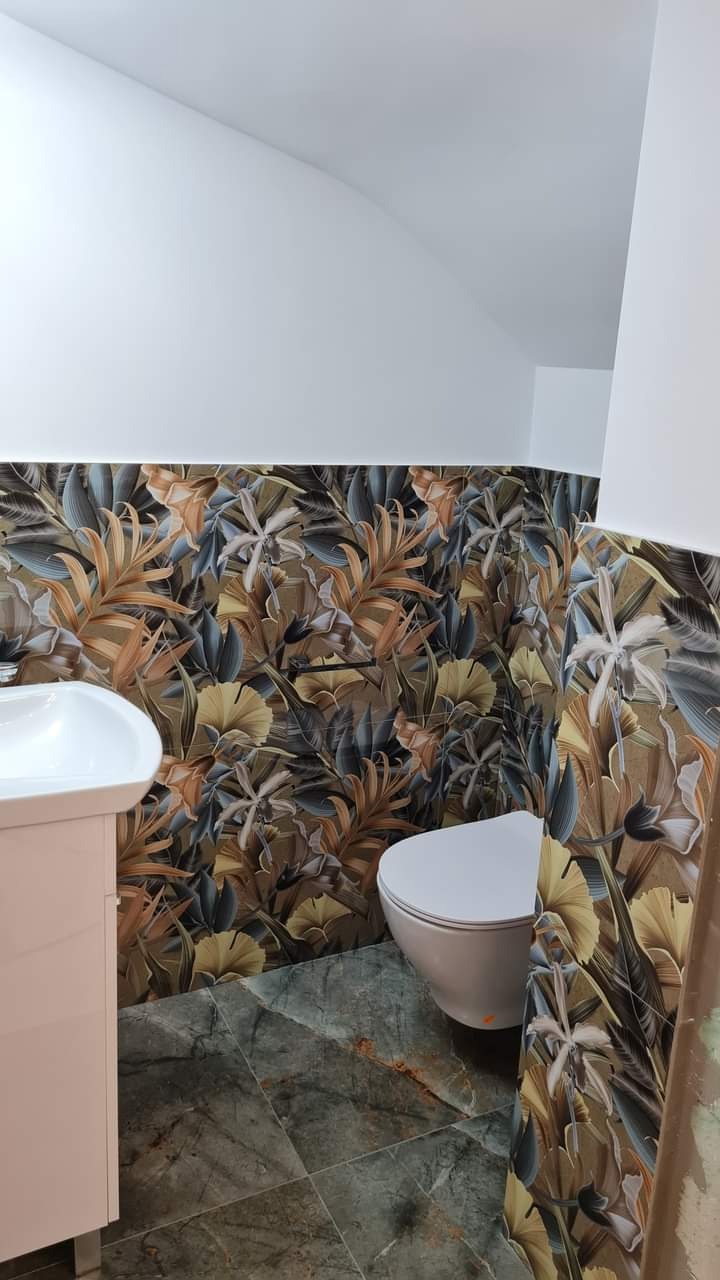 Wykończona łazienka z toaletą, umywalką i płytkami w kwiatowy wzór na ścianach oraz szare płytki na podłodze. Widok na fragment łazienki.